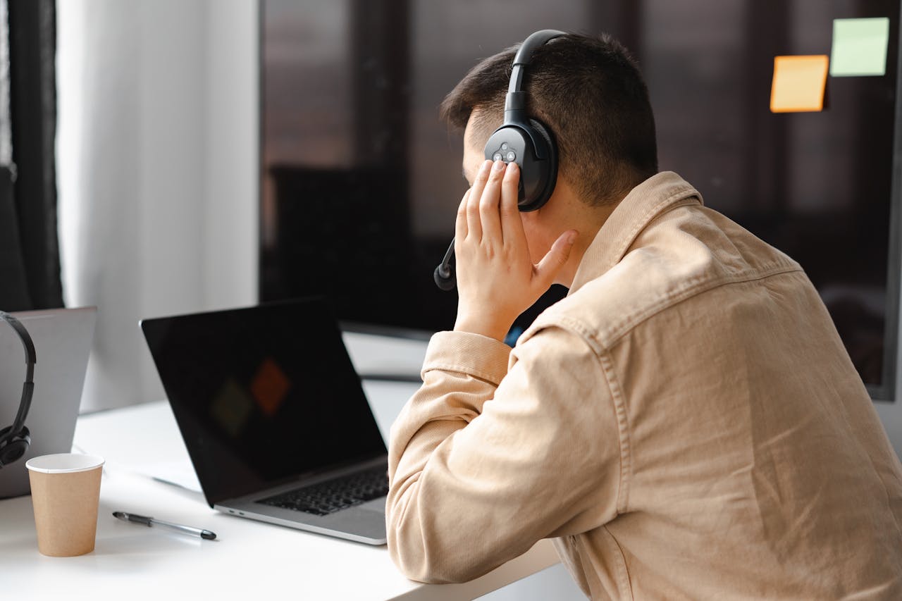 about-us A man wearing headphones works at a laptop in a modern office setting.