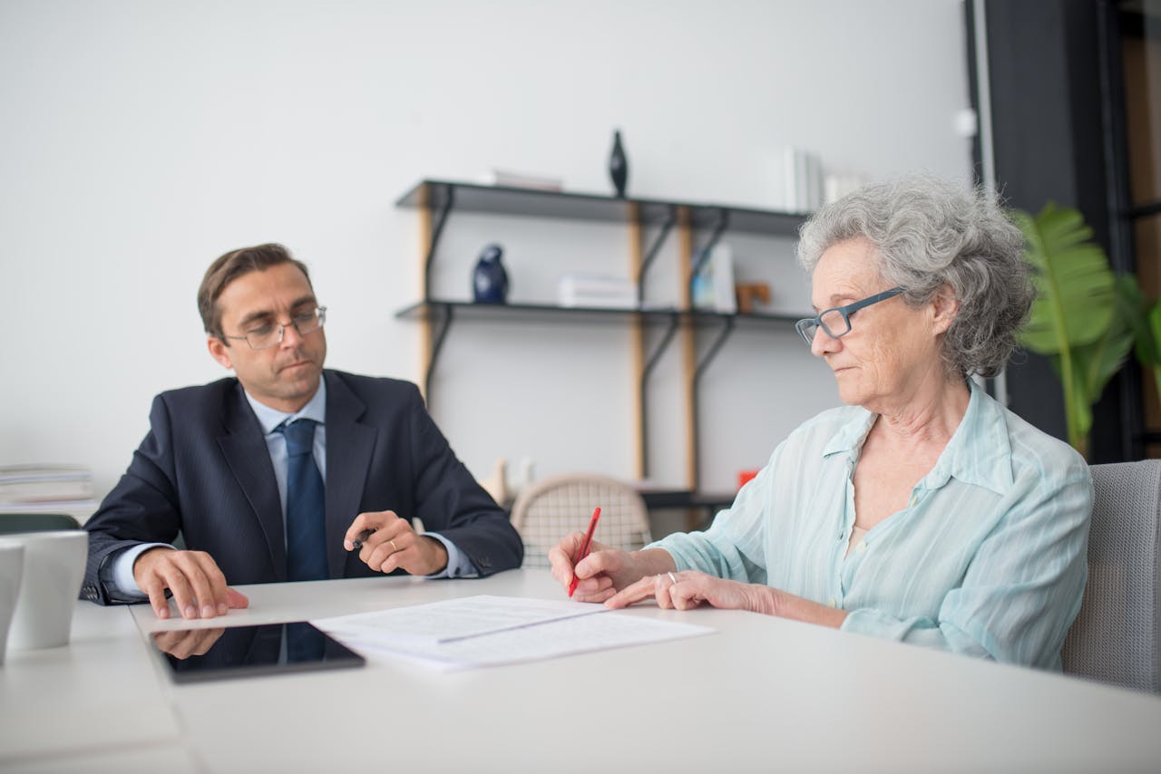 services-03 Elderly woman signing paperwork in modern office with consultant.